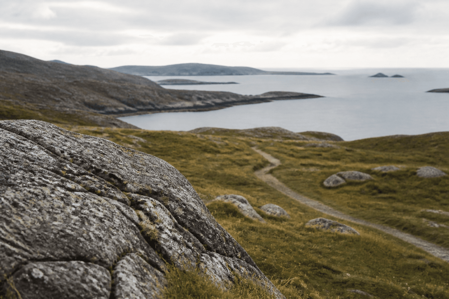 Rock, path and distant sea in a quiet overcast coastal landscape